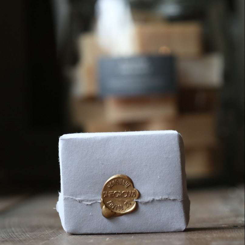 White soap bar with a gold seal on a wooden surface, with blurred background